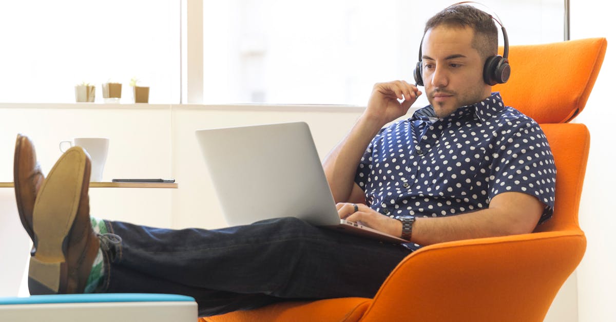 A man relaxes while working remotely in a modern office with a laptop and headphones.